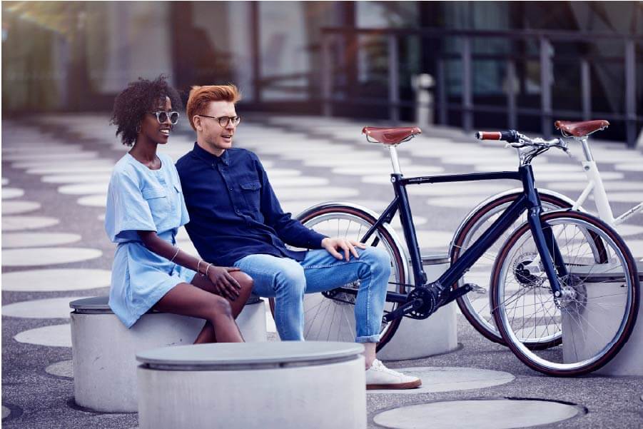 Ein Mann und eine Frau sitzen auf einer Bank und das Fahrrad Schindelhauer Arthur in Farbe mitternachtsblau ist neben ihnen abgestellt